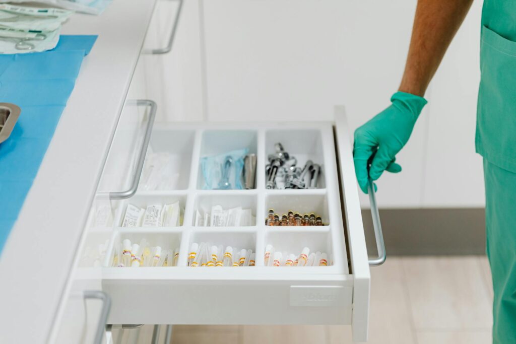Healthcare worker opening a drawer organized with medical supplies and ampoules.