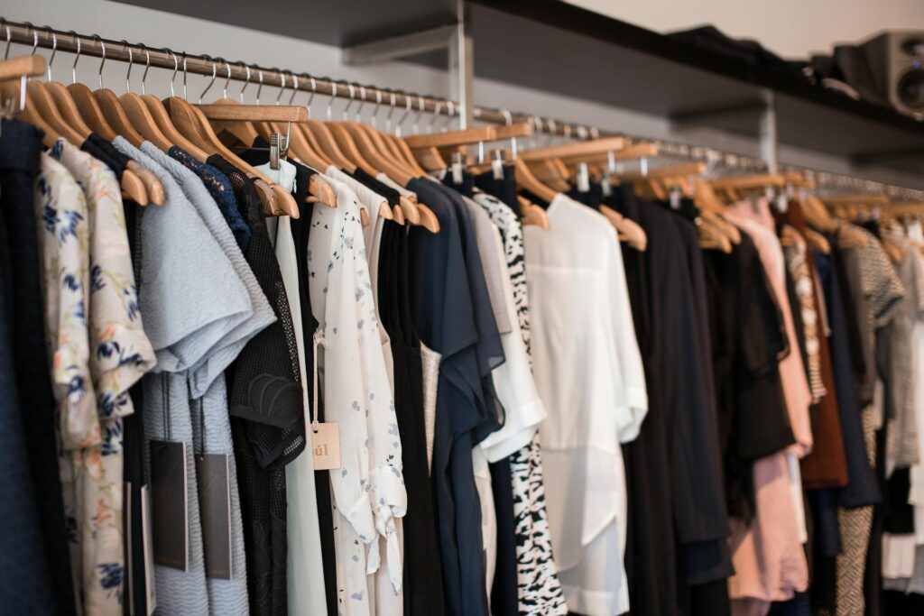 Clothing rack with assorted dresses and tops on wooden hangers in a boutique.