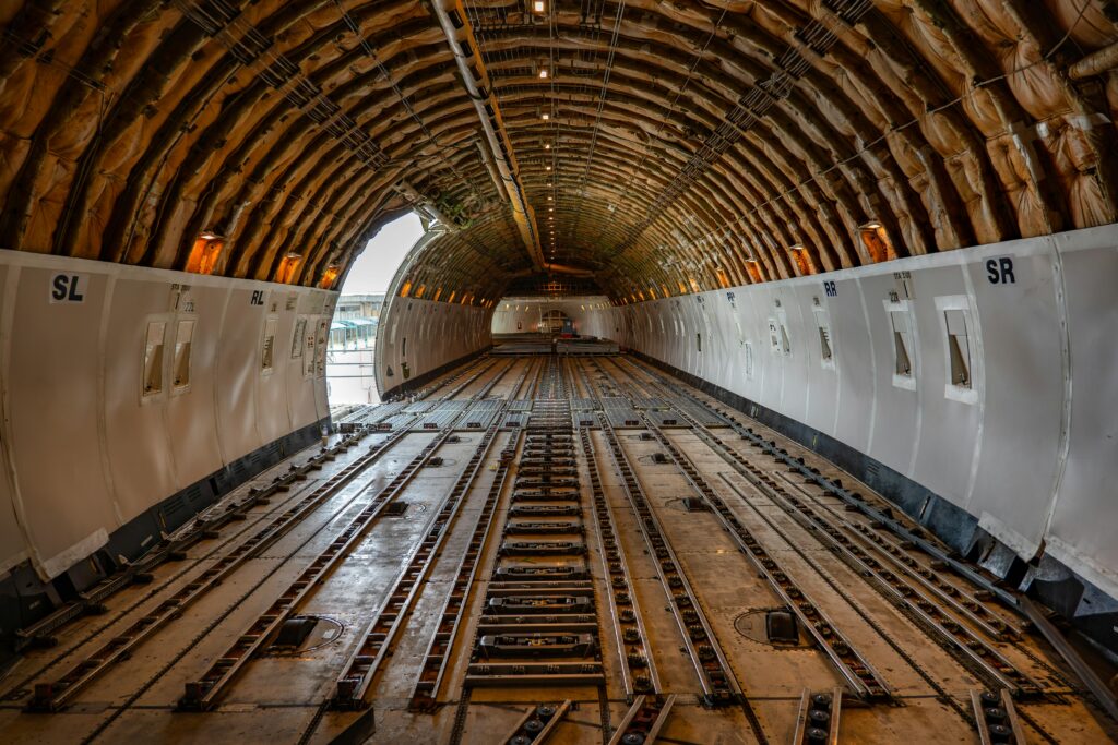 Wide-angle view of an empty cargo aircraft interior, showcasing roller tracks and load locks used for securing freight. The image emphasizes air cargo logistics, capacity, and specialized infrastructure for global shipping.