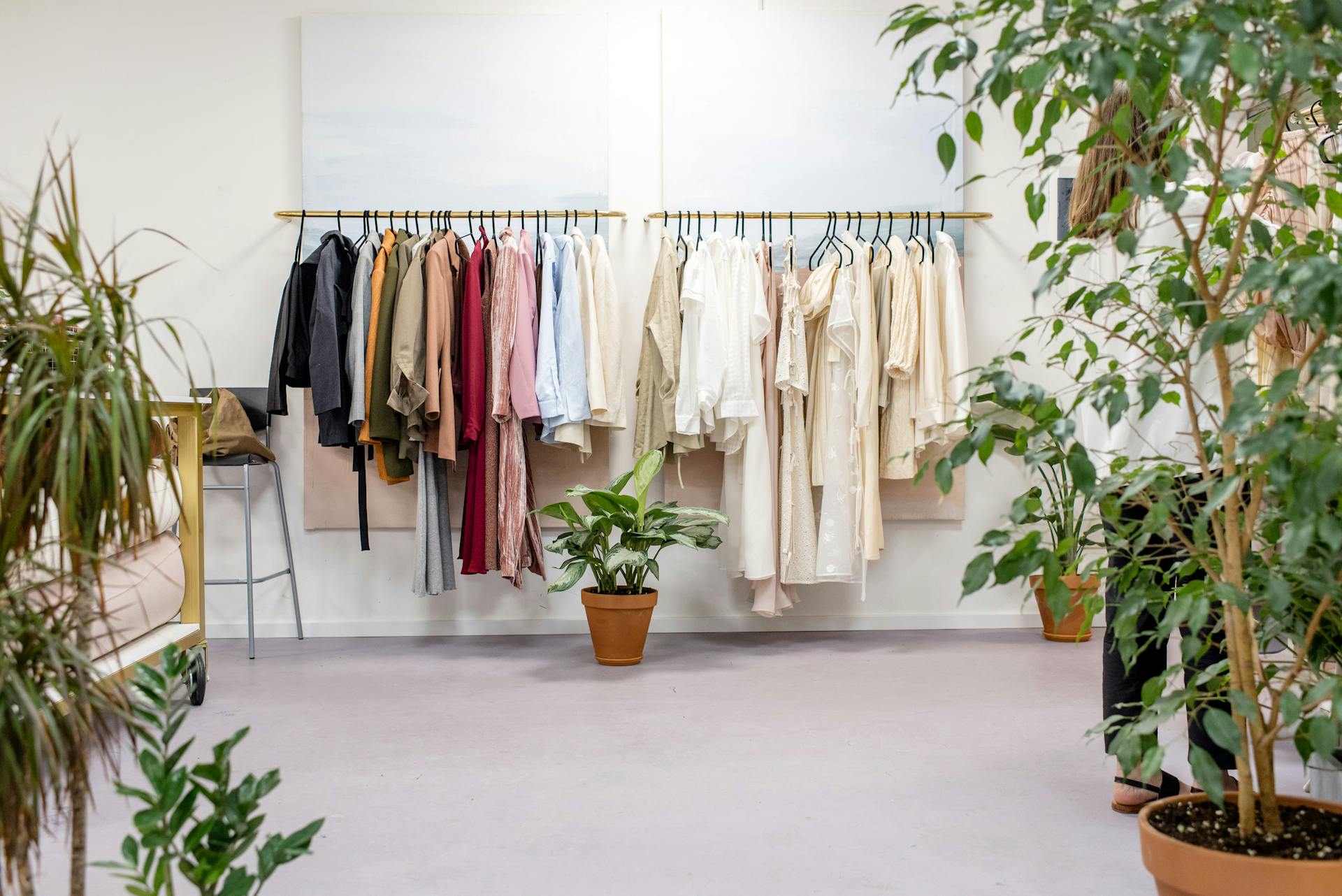 Minimalist boutique clothing racks with neutral and earth-toned garments surrounded by indoor plants.