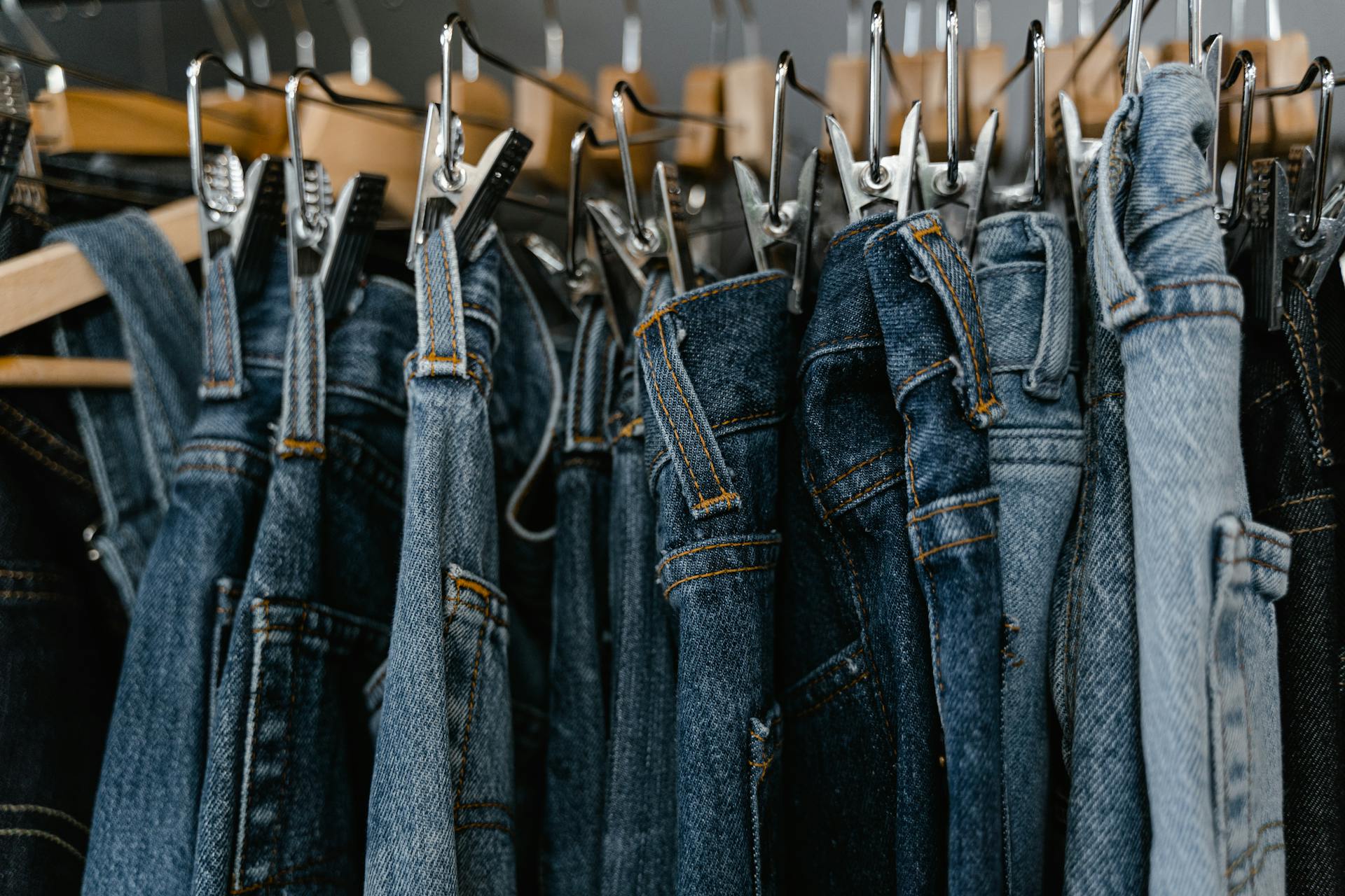 Close-up of various denim jeans hanging on clip hangers.