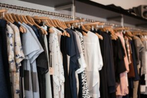 Clothing rack with assorted dresses and tops on wooden hangers in a boutique.